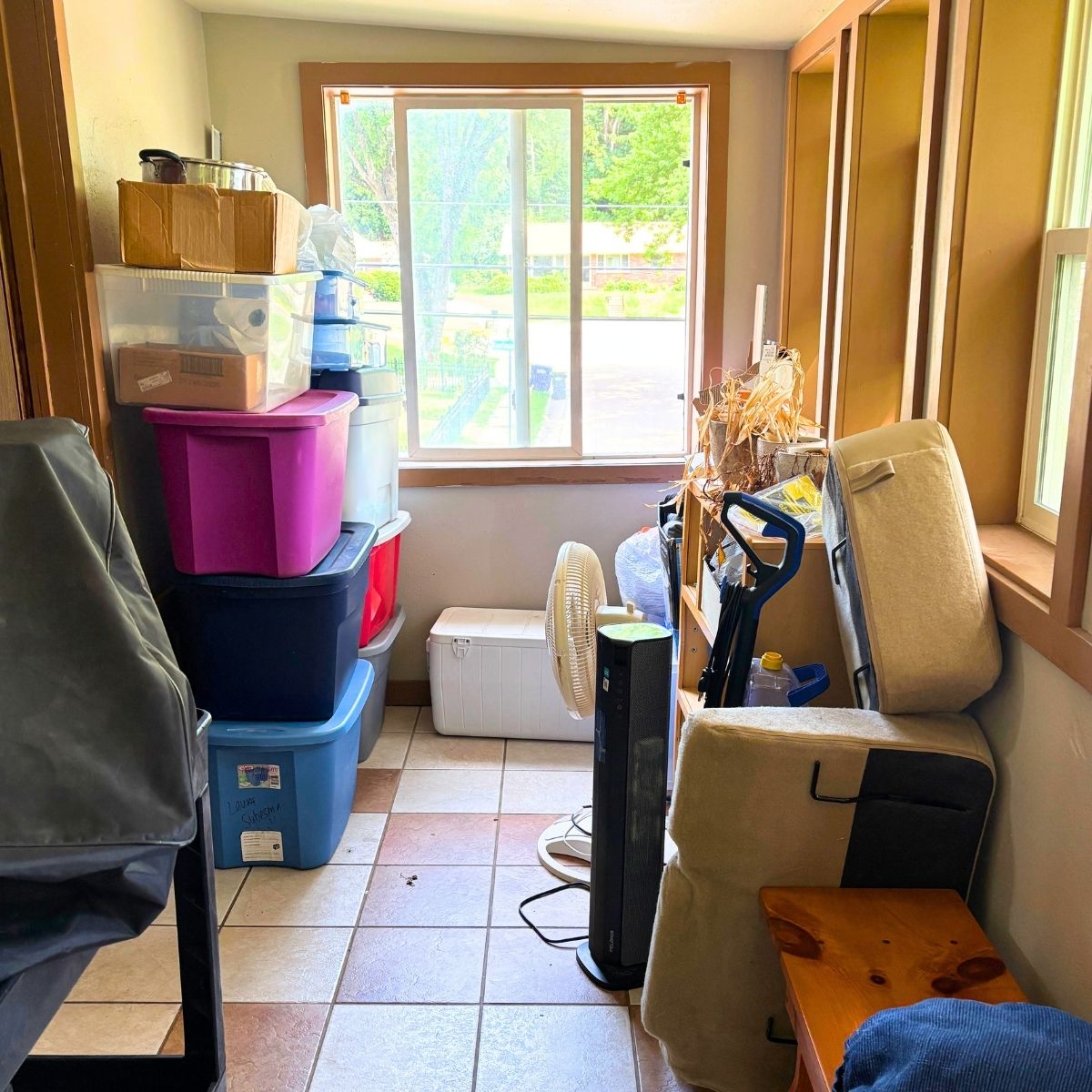cluttered room filled with plastic tubs, old plants, and various furniture