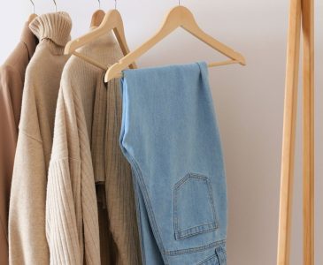 capsule wardrobe of sweaters and jeans hanging from a free standing wooden clothing rack