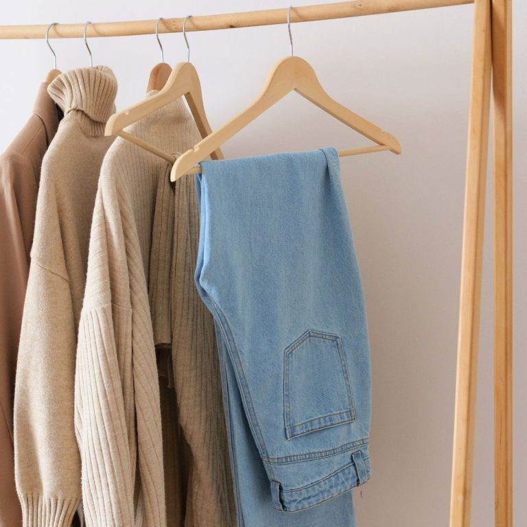 capsule wardrobe of sweaters and jeans hanging from a free standing wooden clothing rack