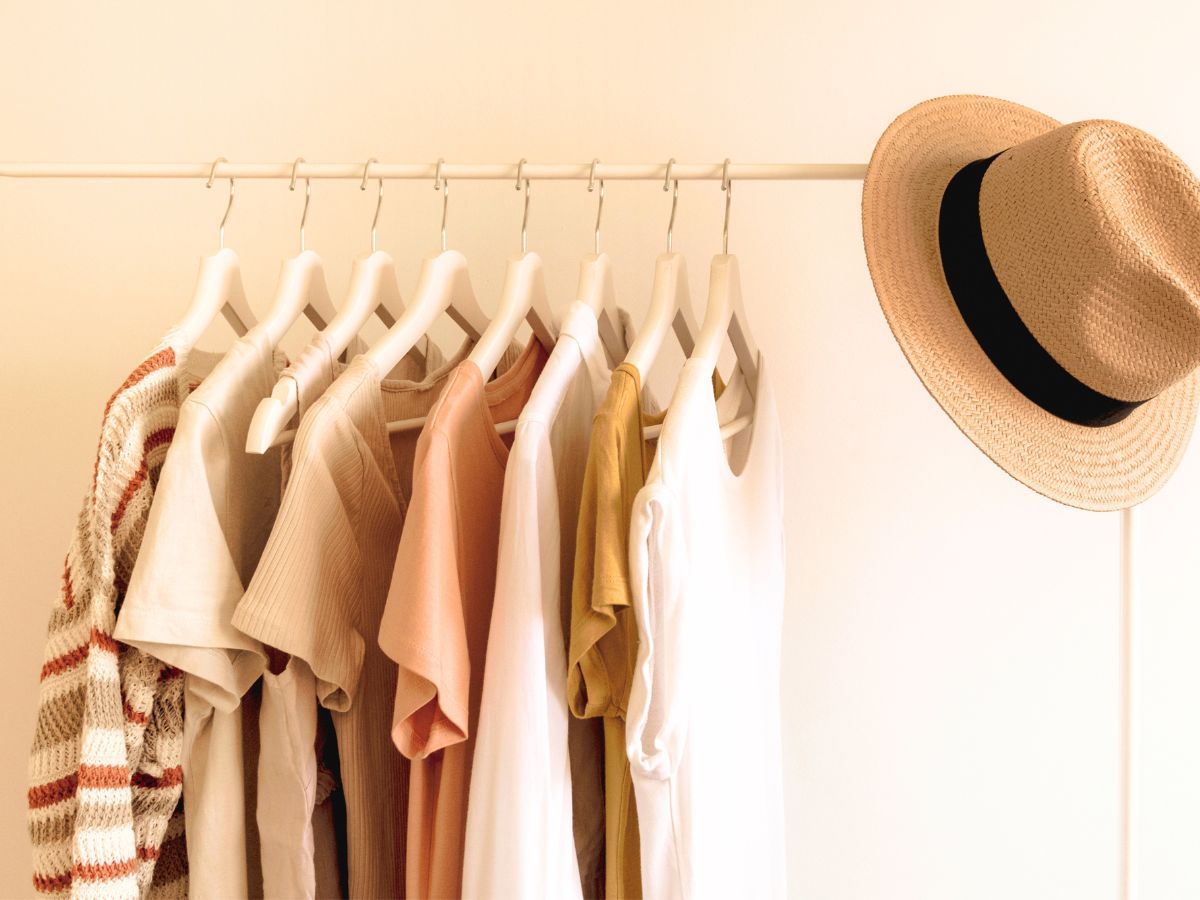 capsule wardrobe hanging on a clothing rack with a straw hat