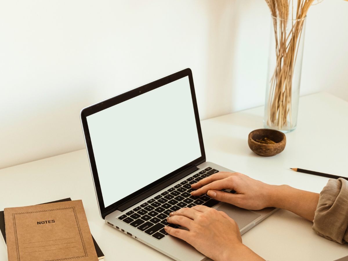woman's hands typing at a computer that is sitting on a desk with notebooks an a pencil