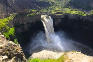 rushing waterfall coming out of a rocky canyon with green grass