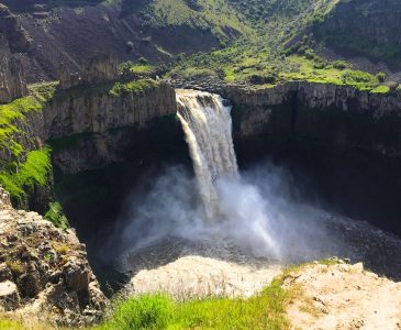 rushing waterfall coming out of a rocky canyon with green grass
