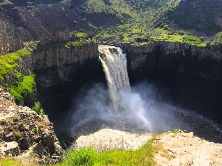 rushing waterfall coming out of a rocky canyon with green grass