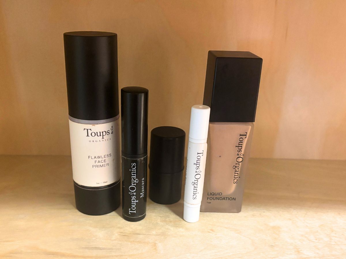 minimalist non-toxic skincare products such as foundation blush and tinted lip balm sitting on a wooden bathroom shelf