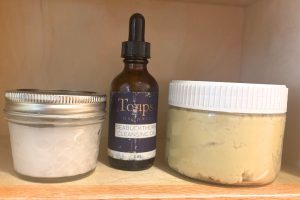 two glass jars with an opaque glass bottle between them on a wooden shelf containing non-toxic skincare products